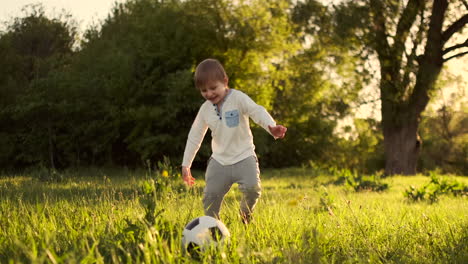 Happy-boy-running-with-soccer-ball-running-at-sunset-in-summer-field.